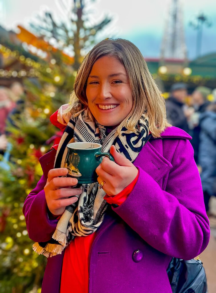  a mug of mulled cider with a christmas tree in the background. 