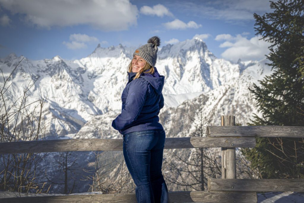 Woman standing in front of a snowcapped mountain wtih a blue jacket and jeans on.