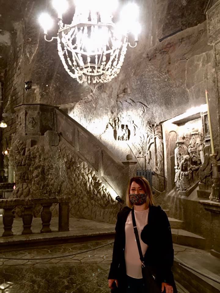 woman in pink shirt and black jacket standing in front of a chandelier in the salt mines in krakow