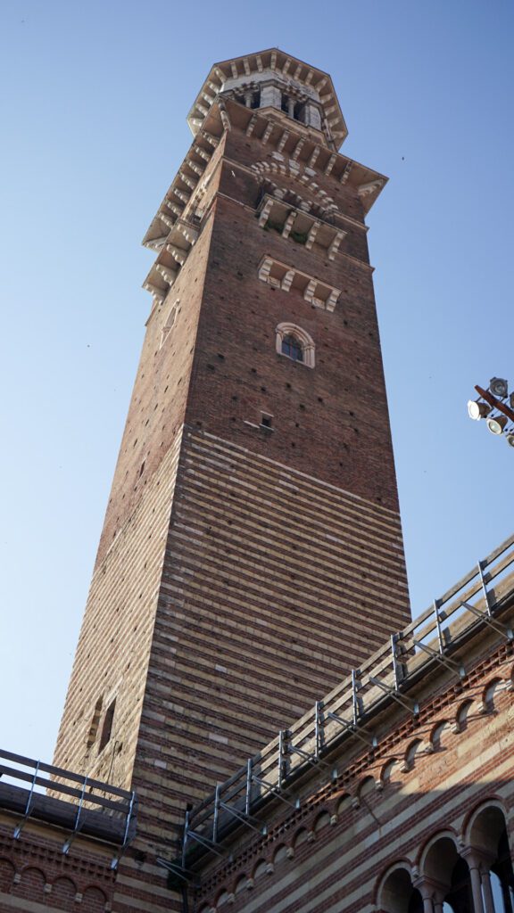 Torre dei Lamberti in Verona italy stands tall with its red and white brick against the blue sky