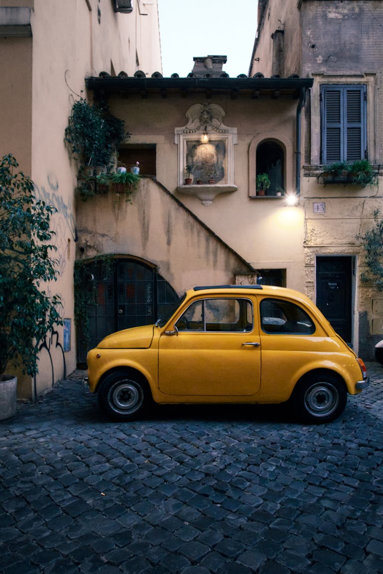 Discover the charm of Rome's streets with this classic yellow car parked by a rustic building.