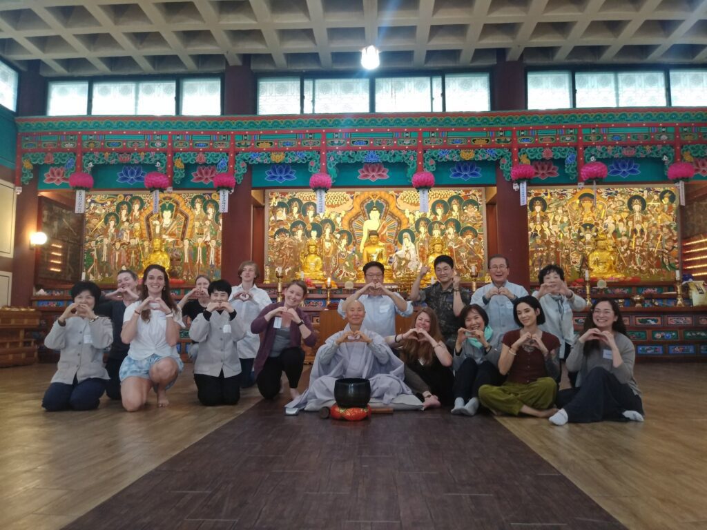 Several people posing with a buddhist monk in a temple in Korea doing the korean heart symbol