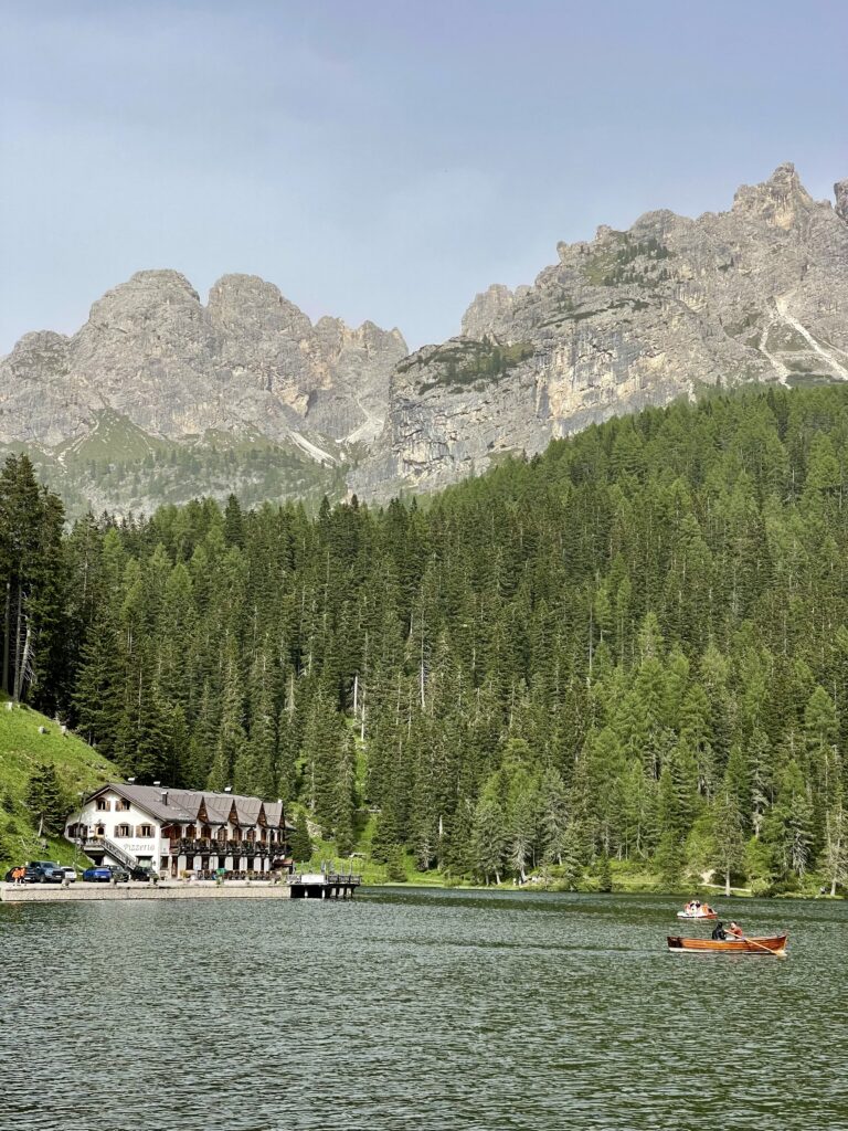 Lago di Misurina sits below the famous Tre Cime Di Lavaredo in the Dolomites. Green trees frame the lake on a bright and beautiful summer day
