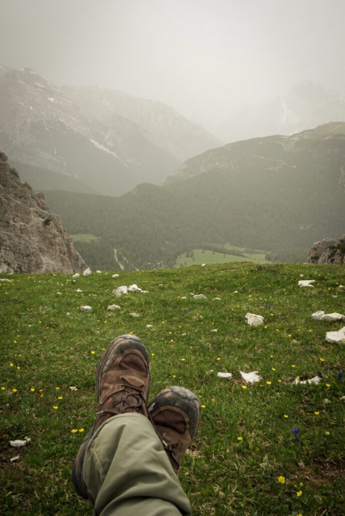 a person sitting on the grass near the Cadni Di Misurnia Look out point . The grass is green, the sky is cloudy