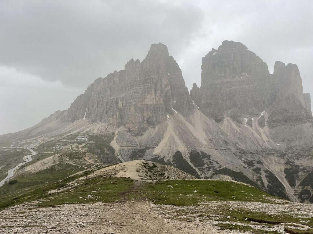 Mountain peaks jutt out into the sky and are surrounded by green grass and gravel