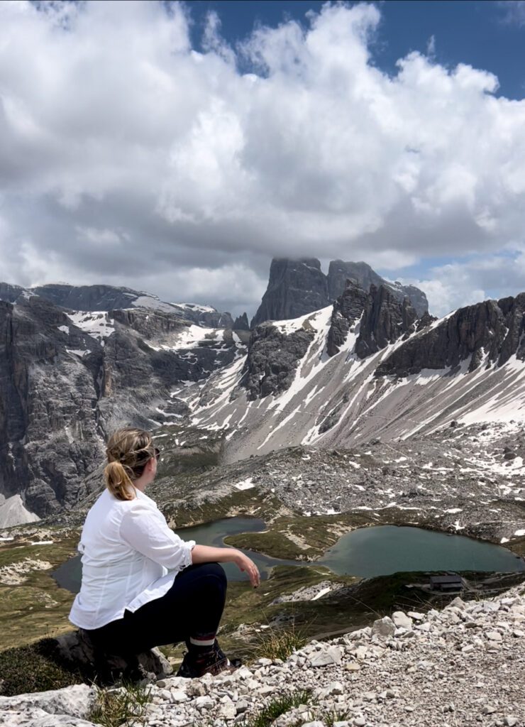 Woman sitting on ground with a view of lakes in front of her.
