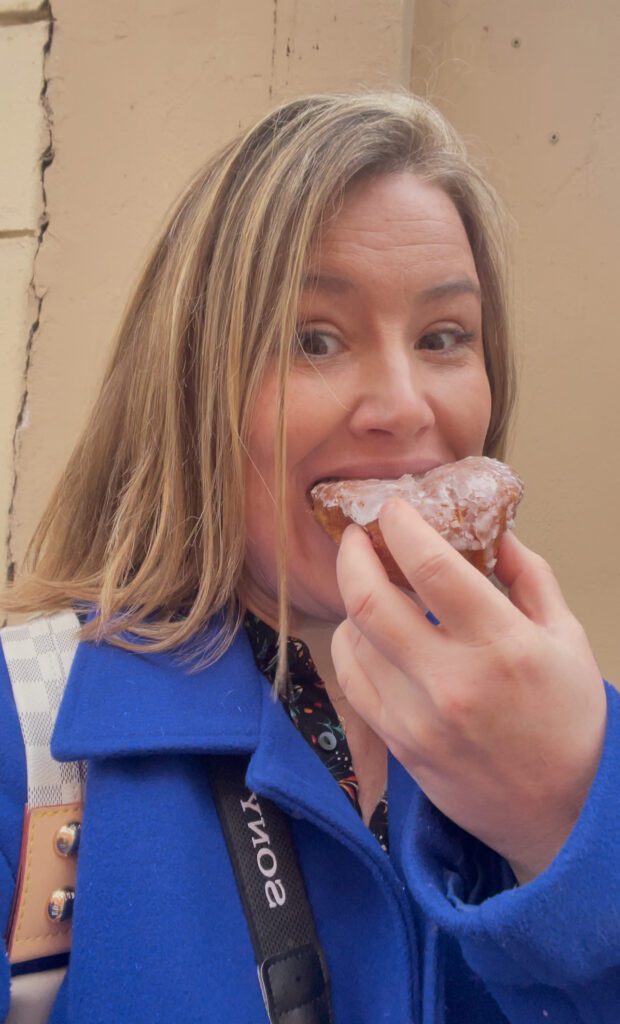 woman with a blue jacket and blonde hair holding a donut in her hand