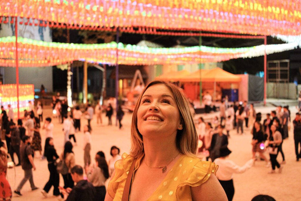 woman looking up at lanterns and bathed in golden glow with people behind her