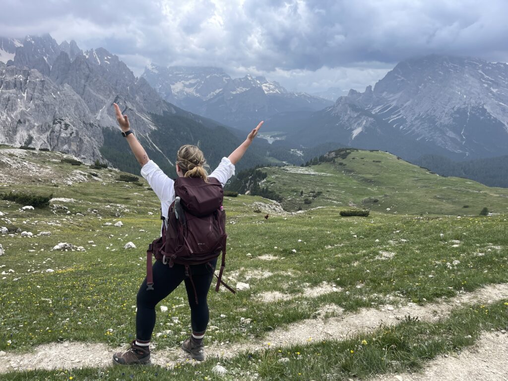 Woman with red backpack and arms outstretched at a vista in the Dolomites on the Alta Via 1