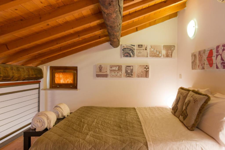 Cozy attic-style bedroom at Hostello in Veronetta with sloped wooden ceilings, a double bed topped with rolled towels and rustic-themed pillows, and vintage art prints decorating the white walls.