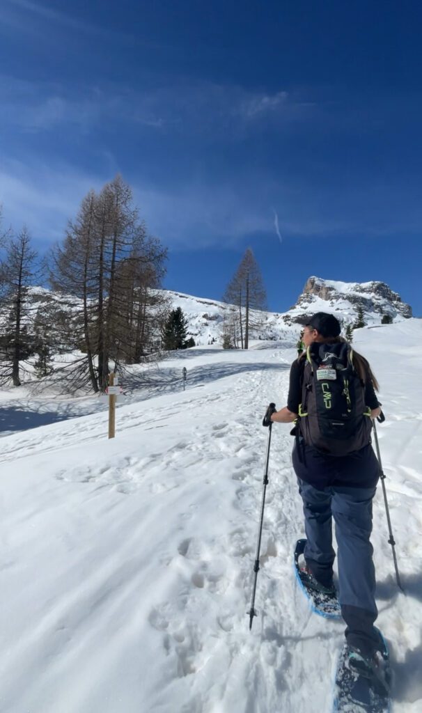 a woman with poles in hands and snowshowing to a the top of the mountain in the Dolomties