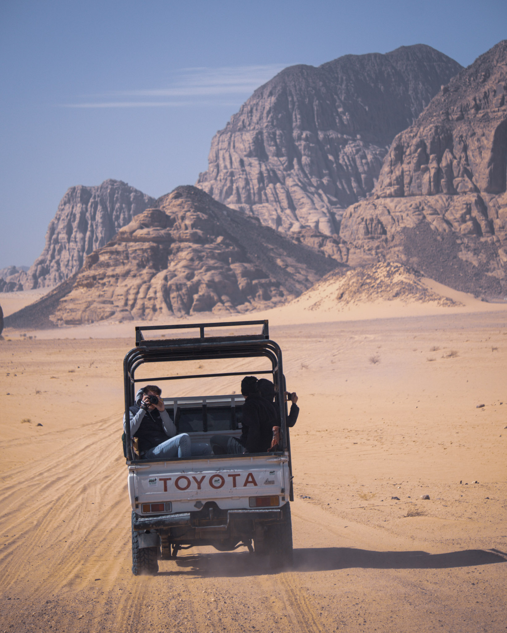 Off-road jeep crossing Wadi Rum desert under towering cliffs