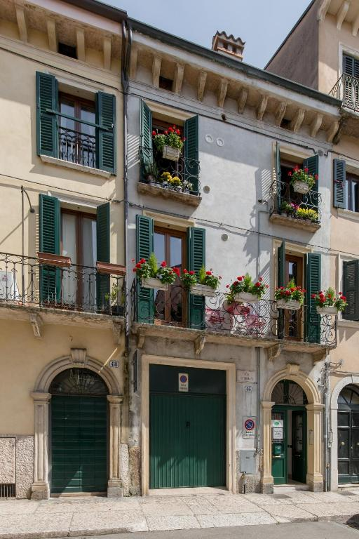 Street view of Veronetta House in Verona showcasing a classic Italian facade with green shutters, flower-filled balconies, and arched doorways on a quiet city street.