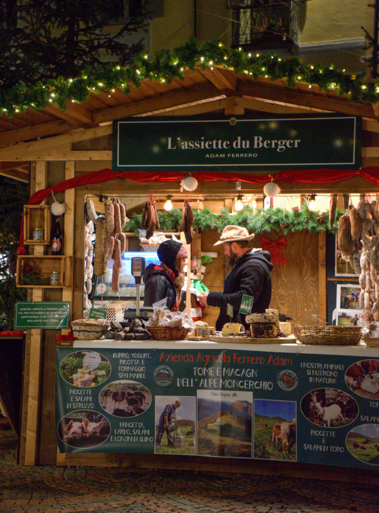 a chalet stall at a christmas market that has mulled wine and various signs in french and italian at the Aosta Christmas Market