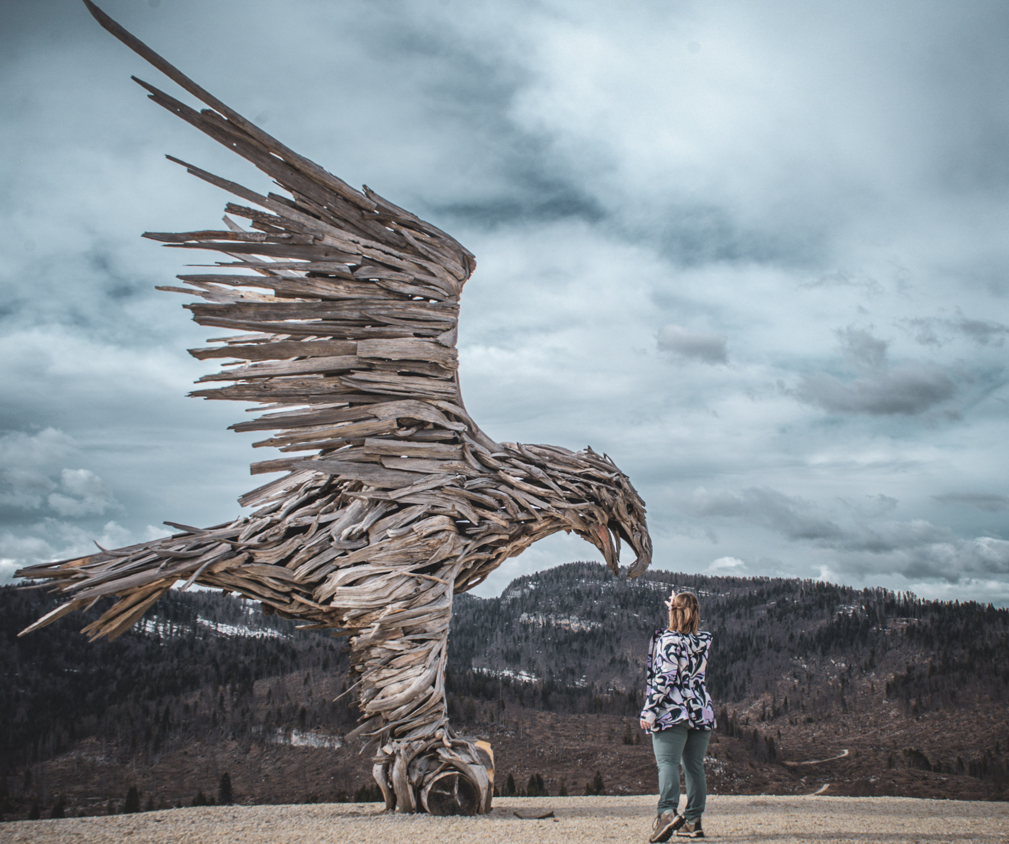 Woman Reaching for Bird made out of wood in an alpine setting against a blue sky