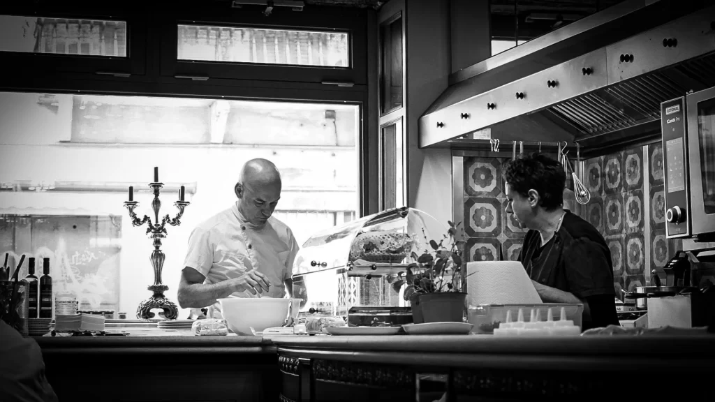 man and woman at a kitchen counter in a restaurant making food, black and white photo