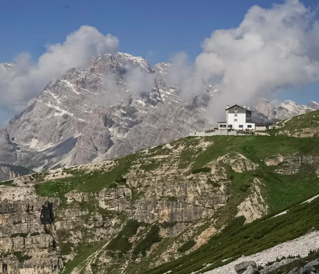 Rifugio Aurunzo in the distance set on a cliffside with clouds rolling in around it
