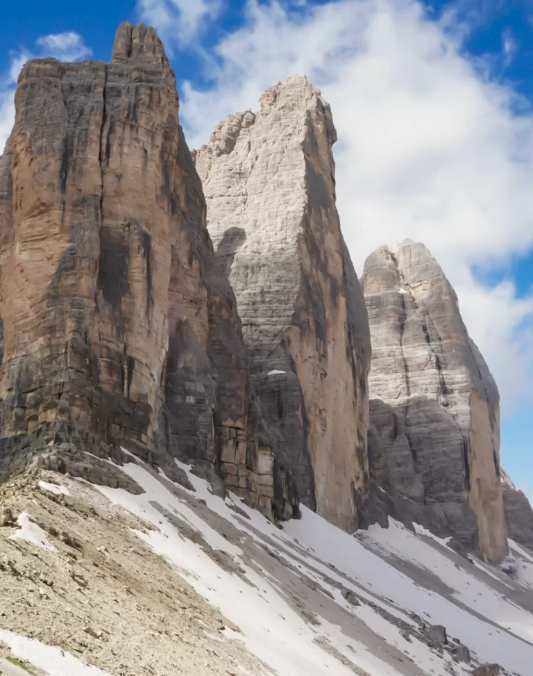 the staggering peaks of Tre Cime Di Lavaredo in the Italian Dolomites. The peaks are grey with a hit of pink and snow lays at it's base.