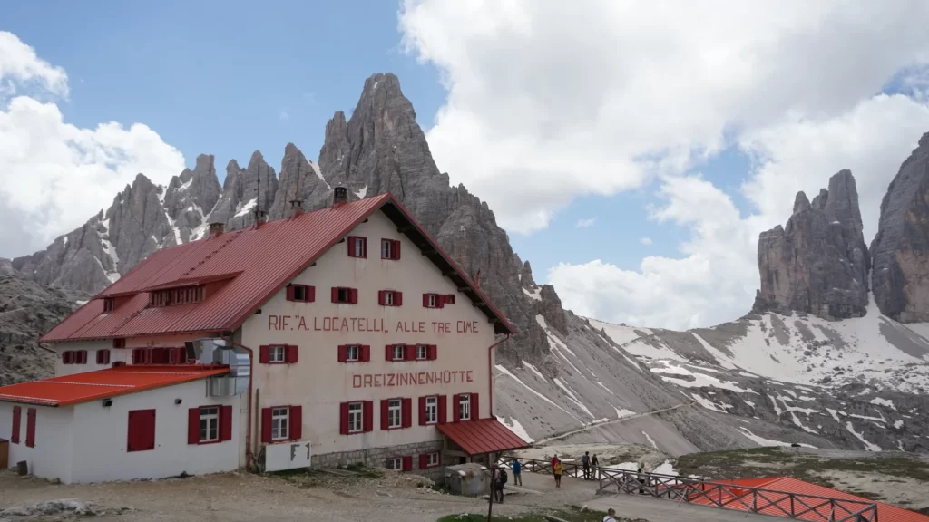 Rifugio Locatelli with one of the three peaks in the background. Skies are blue with clouds swirling above the rifugio