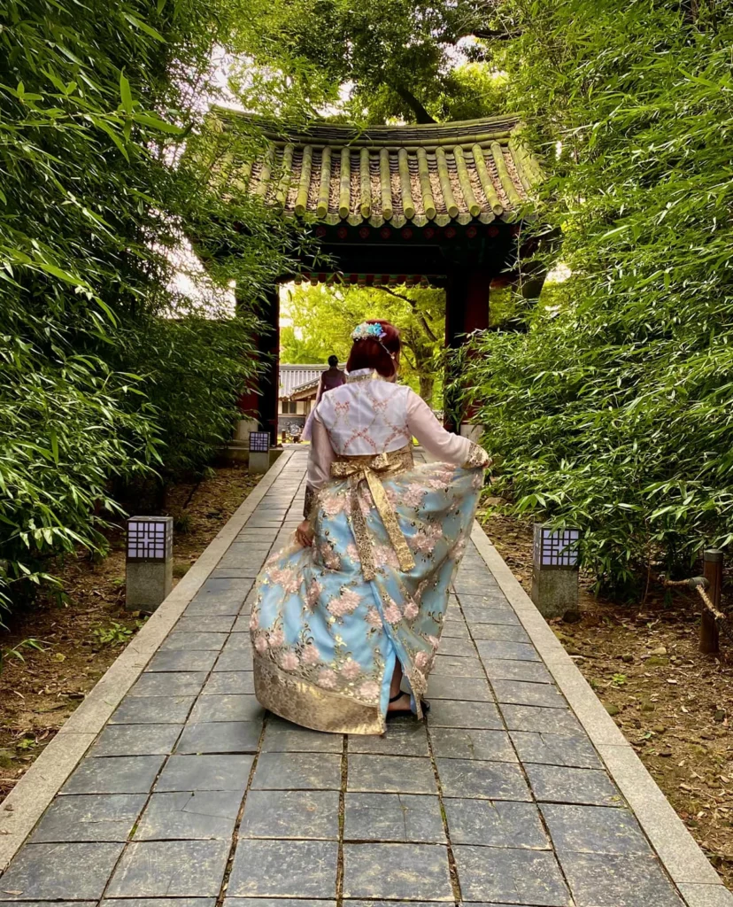 Woman in Hanbok holding her blue skirt up to the side in a pose