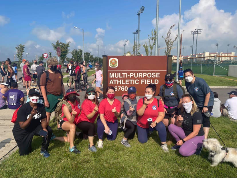 Group of people standing infront of a brown sign that says Camp Huphreys. The group is in athletic gear with the words Humphreys United Club on their Shirts