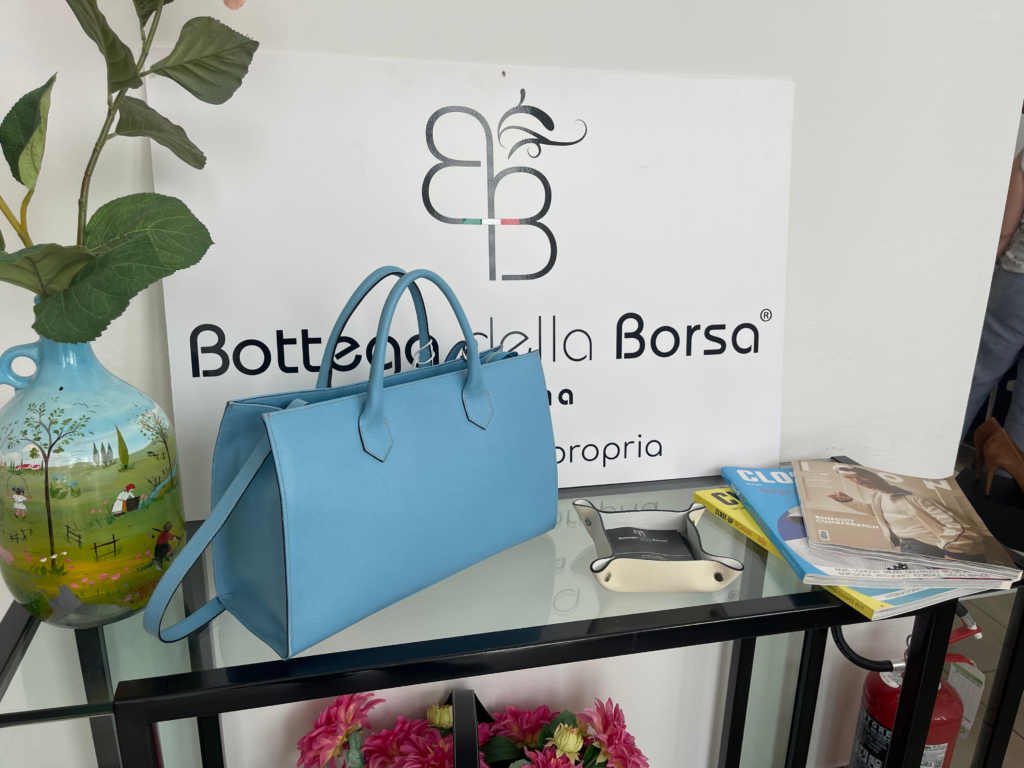 A blue leather purse sits next to a sign in italian Bottega Della Borsa at a shop in Vicenza