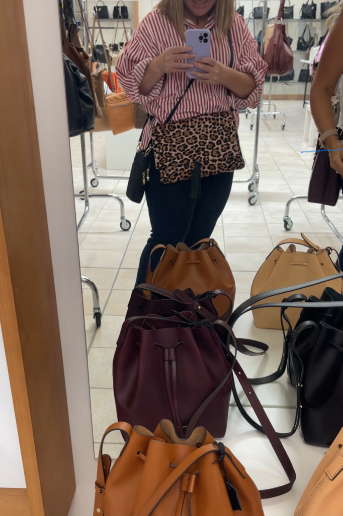 Woman in a red stripped shirt showing off a leopard print purse in front of a mirror