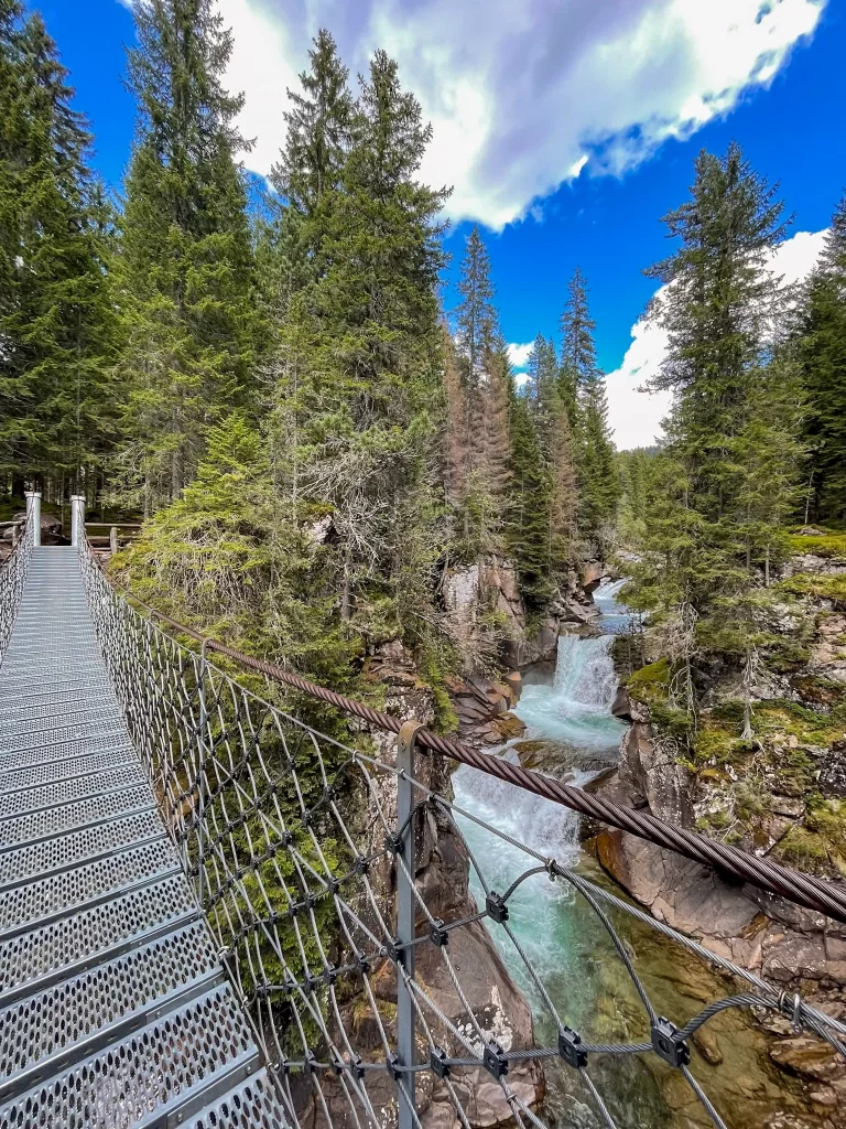 a steel bridge with a waterfall and blue sky over a gorge in the Pale Di San Martino