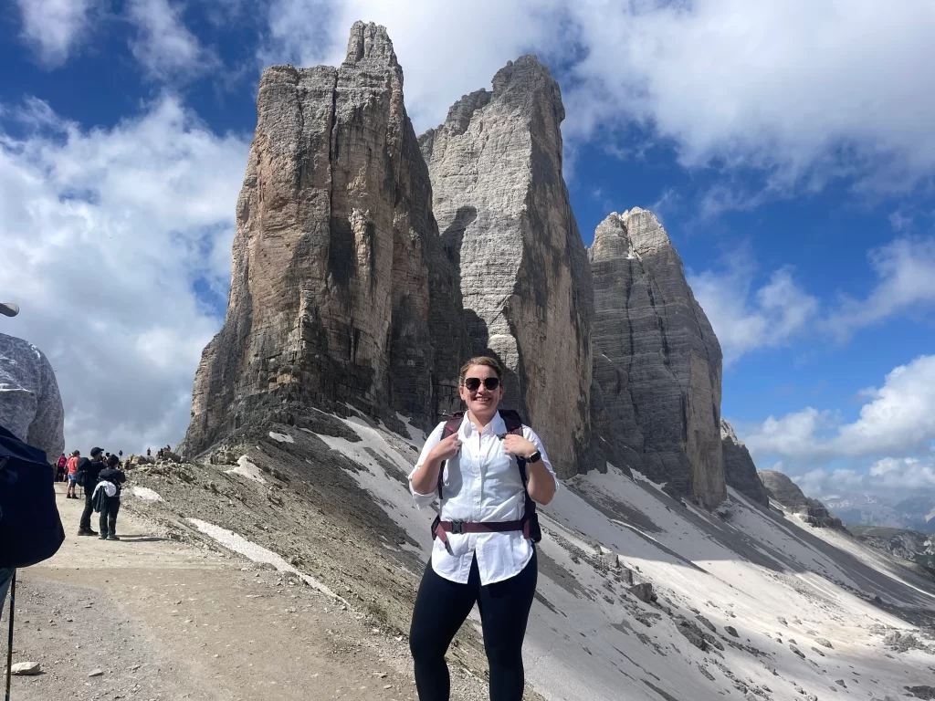a woman in a white top with black pants standing by the three peaks of the dolomites