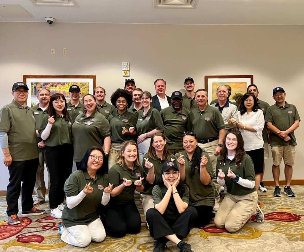 A Group of people with USO logos on their shirts posing for a group photo some of them are doing heart hands in South Korea