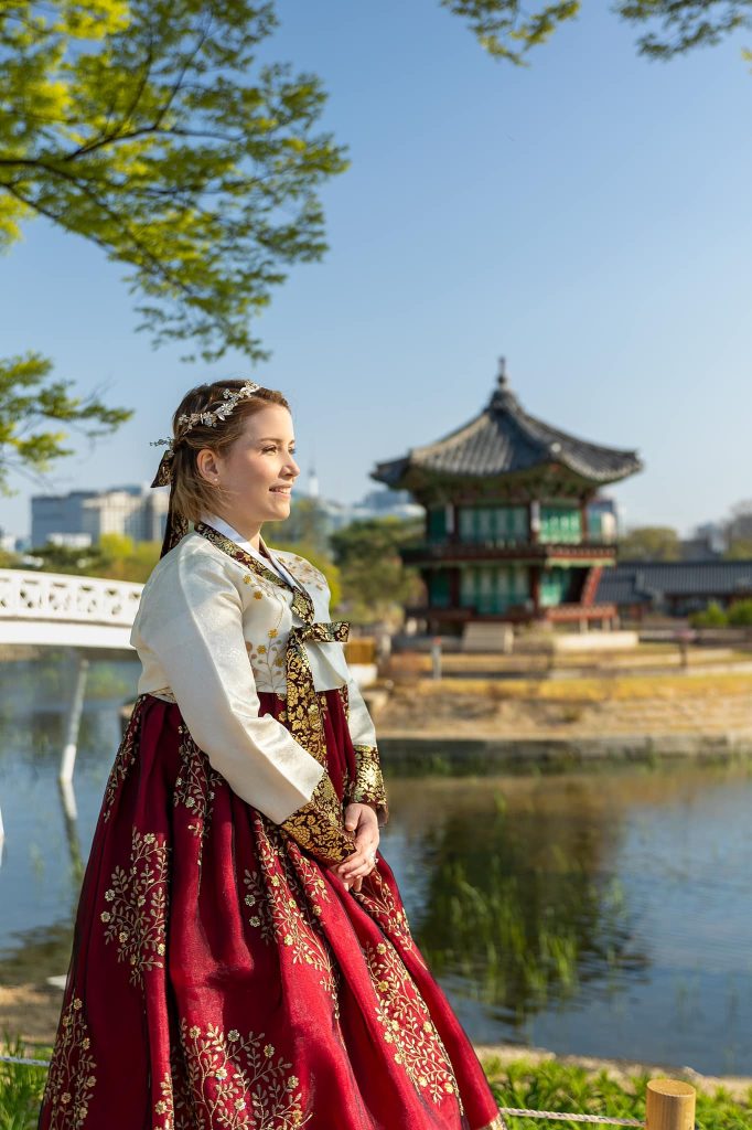 Woman in Traditional Hanbok that is red and white and she is looking off at a temple in Seoul, South Kore