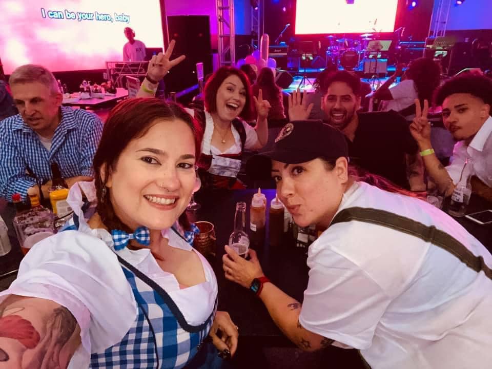 Group of people in a bar in costume. The bar is lit up and says Flightline Camp Humphreys