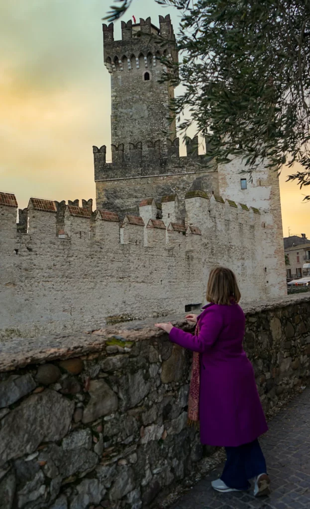 Woman staring at the Sirmione castle in Lake Garda with the sunset behind the castle
