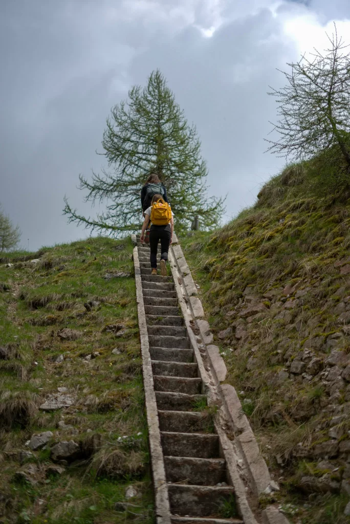 two women walk up the stairs to more ruins. The stairs are concrete and the sky is turnning grey