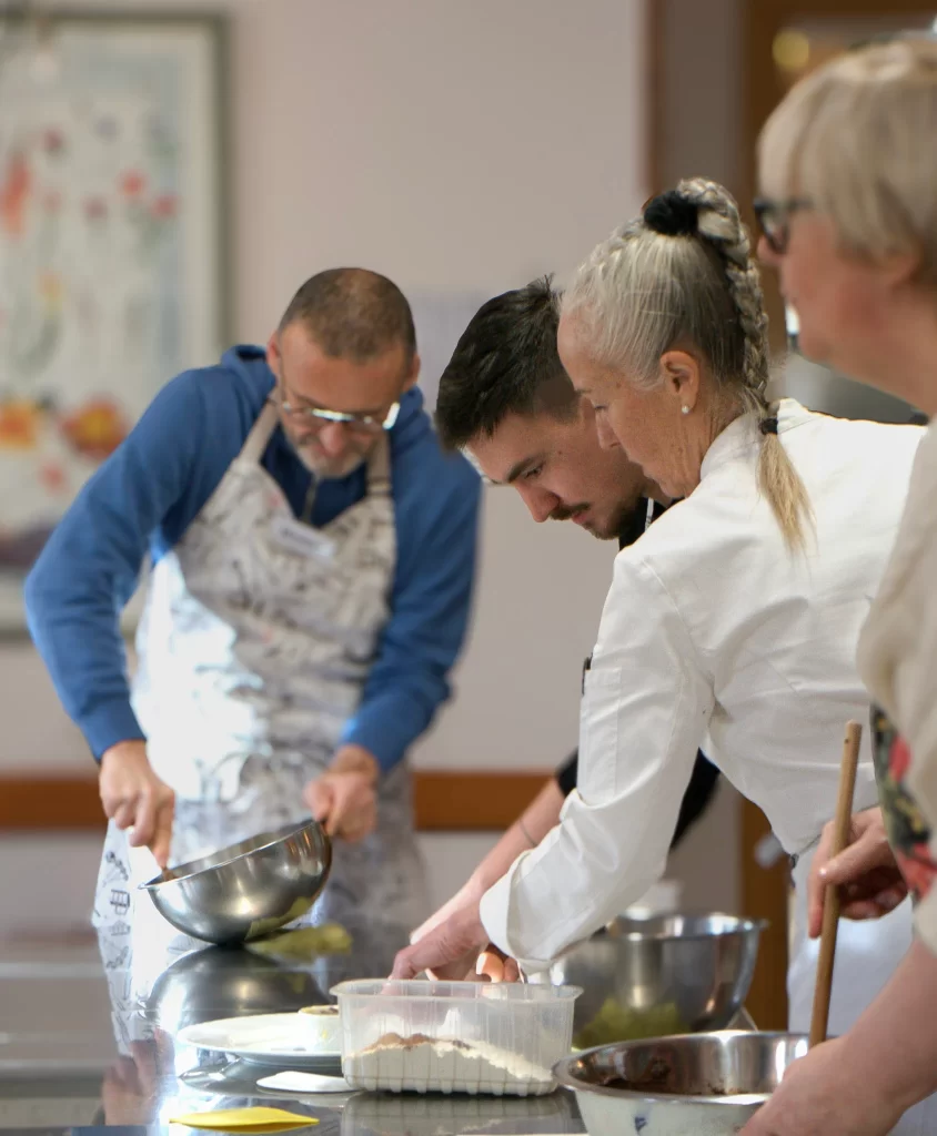 Bari in a white chefs jacket and long grey hair helping students at Trattoria All'Angelo