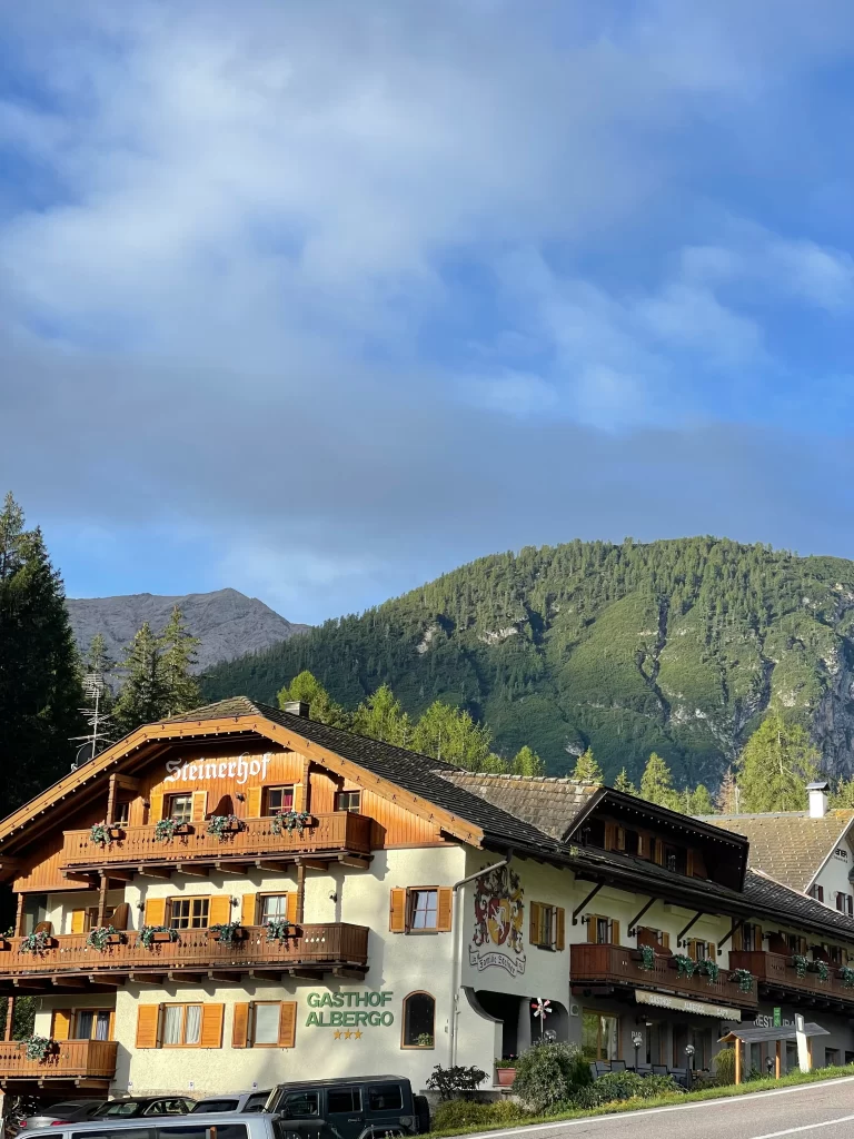 view of a hotel with wooden awnings and mountains in the background. Sun is shining on the hotel