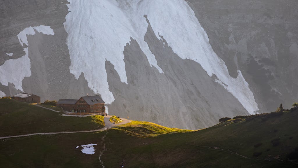 A picturesque alpine shelter bathed in sunset light beneath towering snowy peaks.