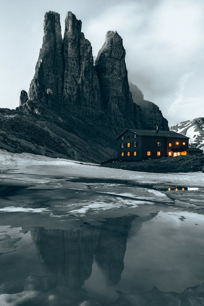 Stunning view of Vajolet Towers in the Dolomites, Italy, reflecting on icy ground with a mountain hut.