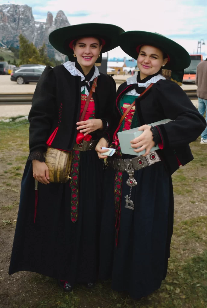 Two women in wide brim black hats and traditional clothing with a barrel in their hand that is full of schnapps at the Compatsch Almabtreib 