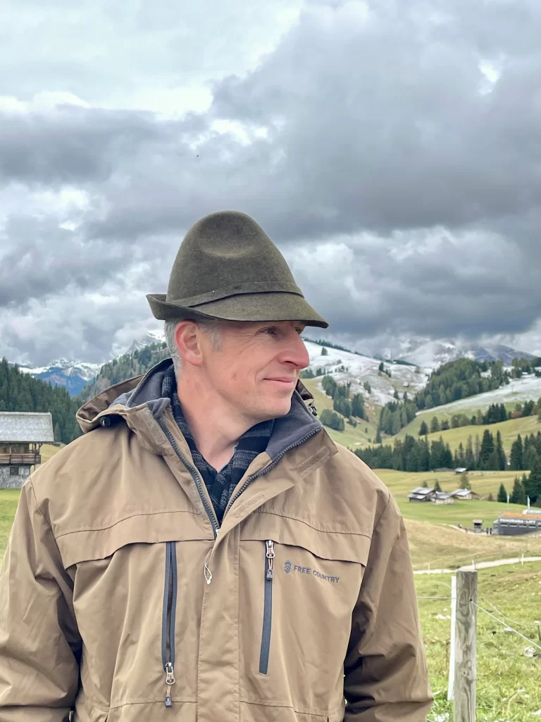 A dashing young man wearing a traditional alpine hat with a brown jacket on in Compatsch