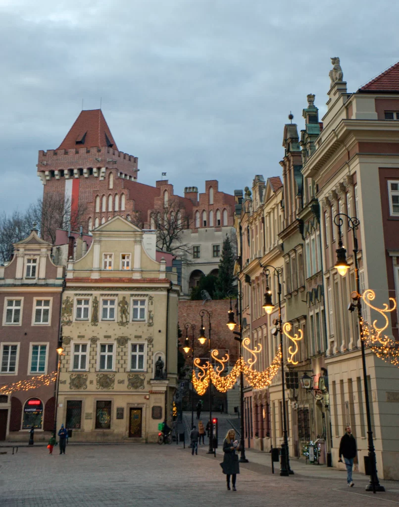 Old medevial buildings in the Stary Rynek of Poznan illuminated in golden light as passerbys walk by