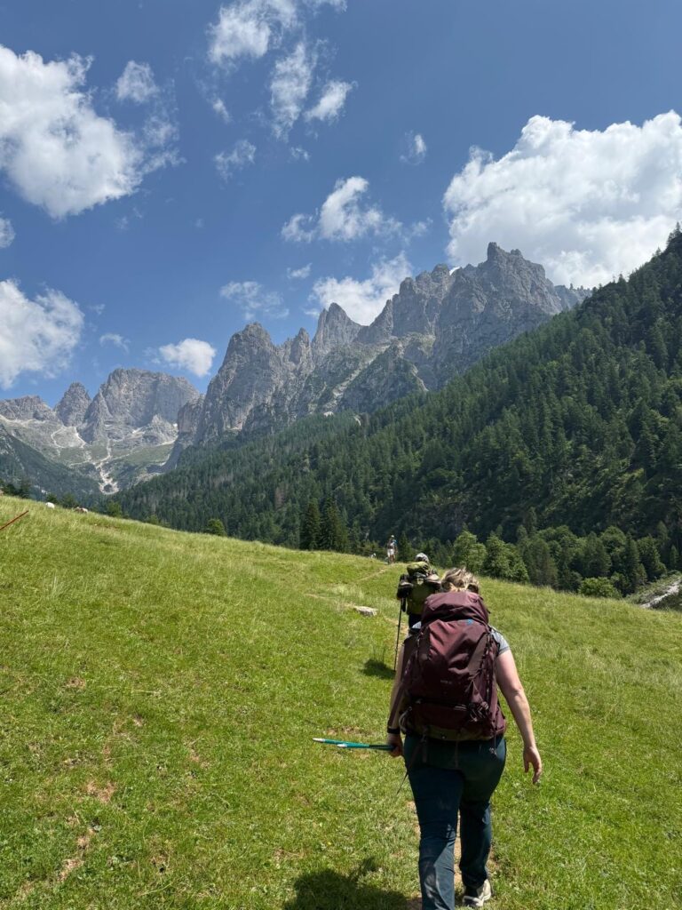 Woman with maroon hiking pack walking through a pasture on the way to Rifugio Treviso