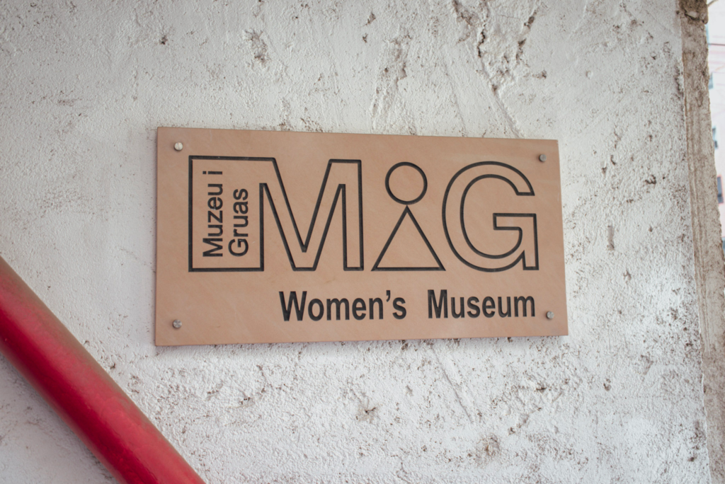 A copper sign on a white wall that says MIG Womens Museum Tirane