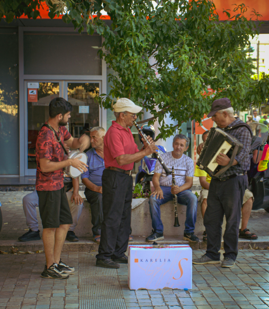 three men standing in a square in Tirana playing instruments like an accordian, flute and tamborine