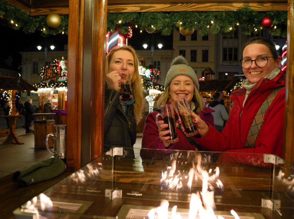 three women holding their christmas mugs up cheersing at a fire pit in the stary rynek in Bydgoszcz Poland