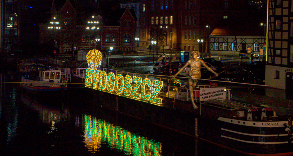 lit up green sign that says Bydgoszcz and a statue of a man on a tightrope