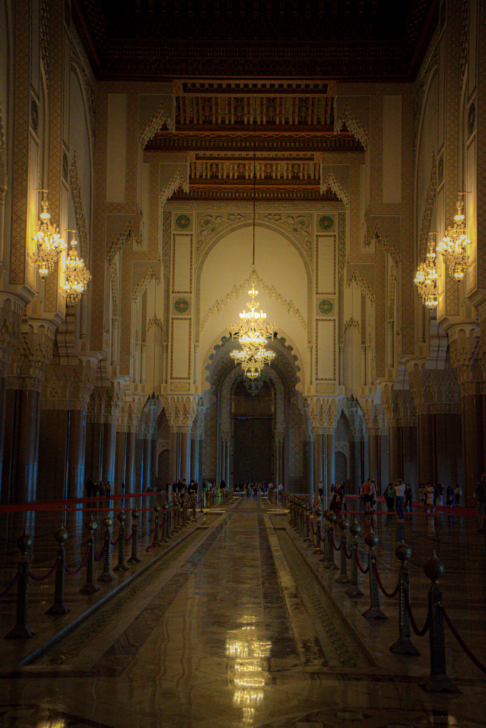 The inside of Hassan II Mosque in low lighting which casts shadows on the walls.