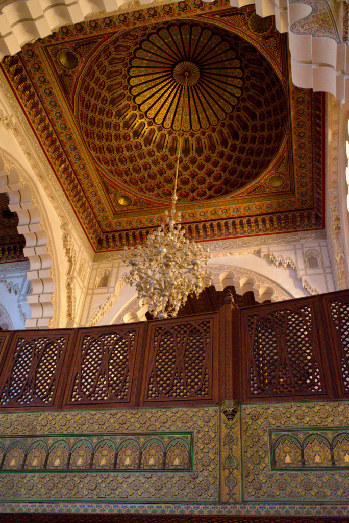The upper levels of the Hassan II Mosque with a large chandelier and intricate wooden railings