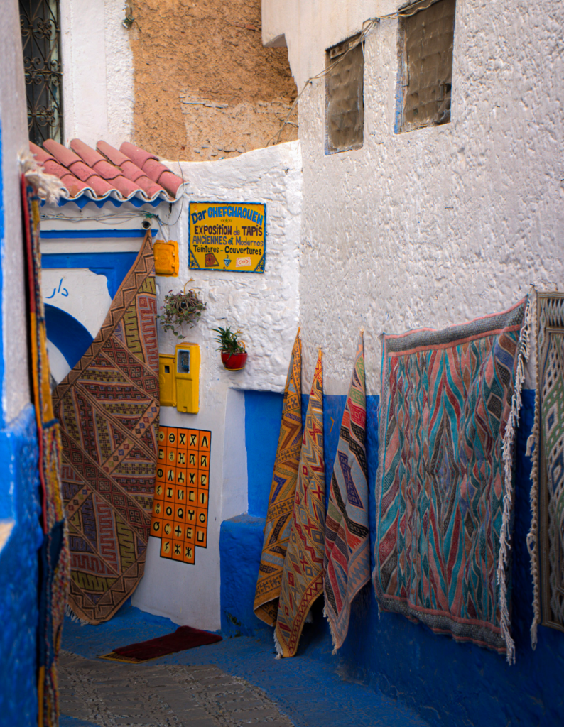 various colorful rugs hanging on a wall in an alleyway in Chefchaouen