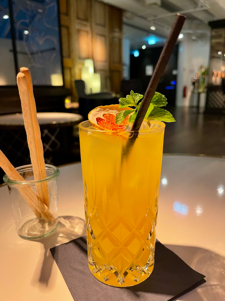 orange mojito with a straw in it and various garnish on a white table